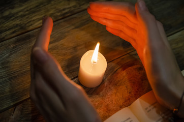Obraz na płótnie Canvas Hands near the candle and a book on the table. Concept of magic, education