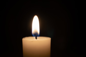 White candle with a flame on a black background close up with copy space