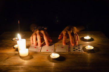 Hands of a fortune teller and cards on the table, around lit candles in the dark on a wooden table....