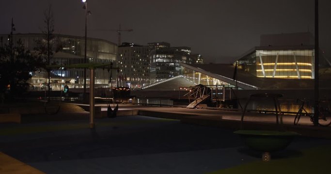 Cinematic wide angle 4K shot with slow parallax motion of illuminated Opera Ballet Theatre and Edvard Munch Lambda gallery with empty playground and swings in front, at night in Bj&oslash;rvika Oslo Norway.