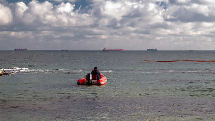 A red rubber coast guard rescue boat with a lifeguard sails to large merchant ships and tankers...