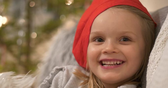Portrait of cute and happy four year old girl In Santa Claus Hat smiling mischievously, Christmas elf concept