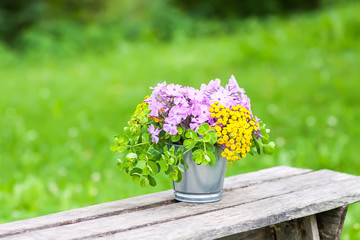 Beautiful bouquet of wildflowers on wooden bench on summer nature background in countryside