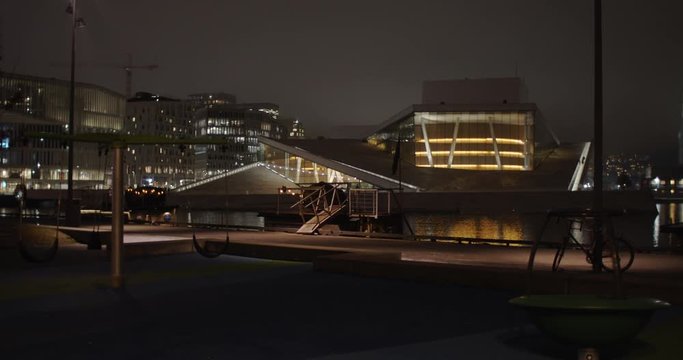 Cinema camera wide angle 4K shot with slow parallax motion of empty dark playground with illuminated Opera Ballet Theatre and Edvard Munch Lambda gallery in background, at night Bj&oslash;rvika Oslo Norway.