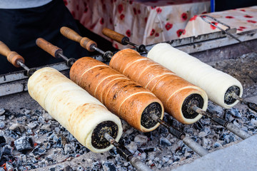 Four fresh Kurtos kalacs (Chimney Cakes) being cooked and glazed with sugar on rolls spinning and displayed for sale at a local Hungarian market stand, traditional food photographed with soft focus