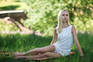 The blonde girl on a meadow. The girl in white sits on a meadow with a plaid. The girl has a rest on a grass.