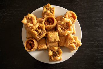 Traditional eastern assorted baklava. Top view. Arabic baked sweets in white plate on dark wooden  table. Baklawa mix 