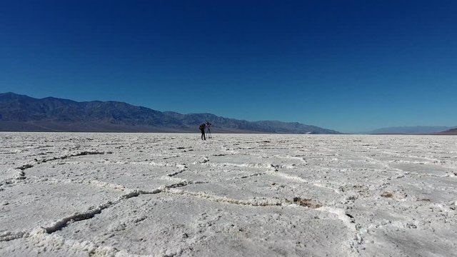 Female traveler with trendy rucksack taking photo of scenic landscape of Badwater basin, photographer hiker in wild environment of Death valley using camera and tripod for taking picture of nature