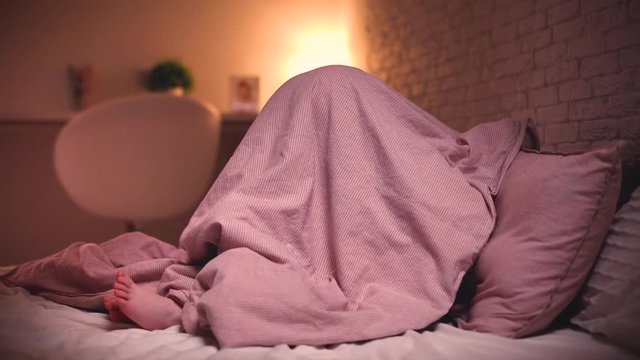 cute little kid hiding under the blanket in bedroom in the evening