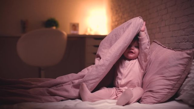 adorable little baby girl playing hide and seek in bed before going to sleep