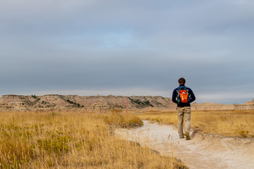 Man Walking Down Path into Panoramic View of Badlands Geological Features