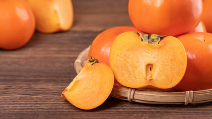 Fresh, beautiful orange color persimmon kaki on bamboo sieve over dark wooden table. Seasonal, traditional fruit of Chinese lunar new year, close up.