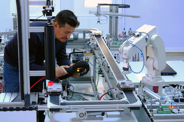 industry 4.0 concept: close-up of an engineer who is teaching robot arm the points with control panel (teach pendant) on smart factory production line. Selective Focus.