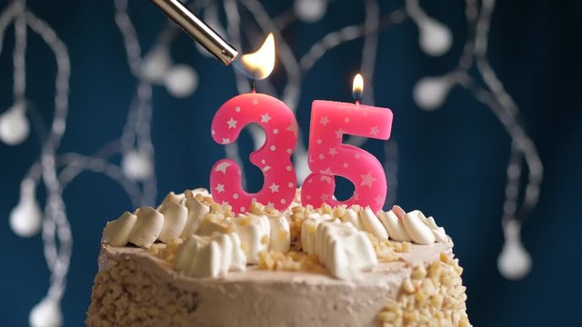 Birthday cake with 35 number pink candle on blue backgraund. Candles are set on fire. Slow motion and close-up view