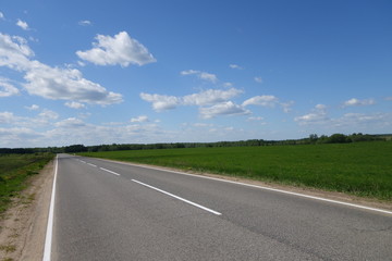 Obraz premium open empty road blue sky with dispersed clouds and green fields