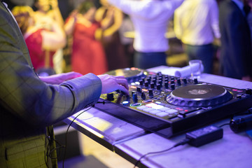 Dj mixing at party festival with crowd of people dancing in background.