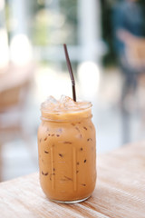 Iced Thai Milk Tea in glass with straw on wooden table in cafe.