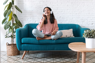 Pretty young woman listening to music with digital tablet and relaxing while sitting on sofa at...