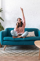 Motivated young woman listening to music with digital tablet while sitting on sofa at home.