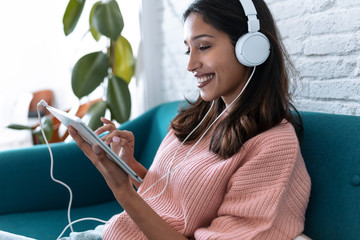 Pretty young woman listening to music with digital tablet while sitting on sofa at home.