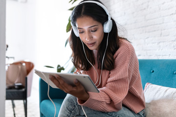 Pretty young woman listening to music with digital tablet while sitting on sofa at home.