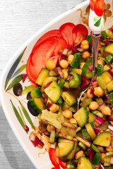 Chickpea salad in olive oil with cucumber, onion, celery, green pepper and seasoning in a patterned bowl with serving spoon and fork