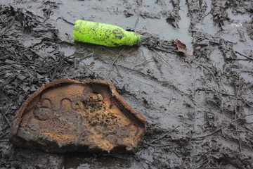 Empty green plastic bottle and other household rubbish used in the mud. Environmental pollution