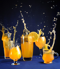 glasses with orange juice with splashes of liquid on a blue background