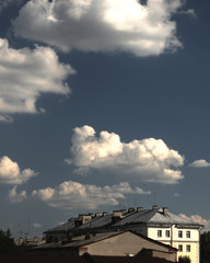 landscape with tops of roofs on a background of blue cloudy summer sky