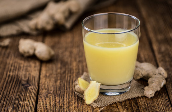 Old wooden table with fresh Ginger Juice (close-up shot; selective focus)