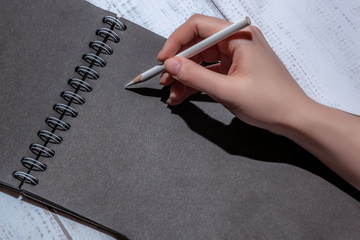 female hand with a white pencil on a black sheet of paper, concept for planning, creativity, to-do...
