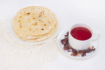 indian chapati bread. chapati on a white plate with a mug of red tea from pomegranate petals on a white background. cooking in a dry pan.