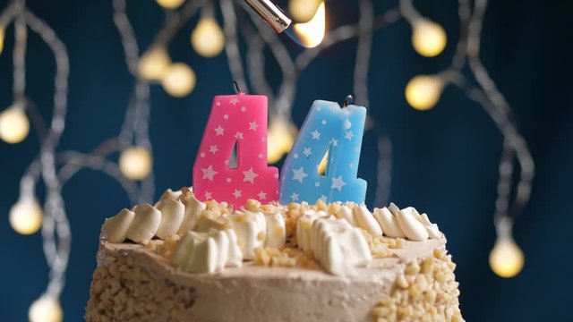 Birthday cake with 44 number pink candle on blue backgraund. Candles are set on fire. Slow motion and close-up view