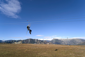 Rear view of young man riding on zip line against blue sky