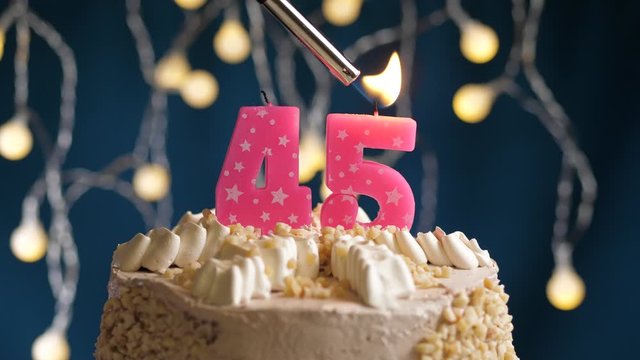 Birthday cake with 45 number pink candle on blue backgraund. Candles are set on fire. Slow motion and close-up view