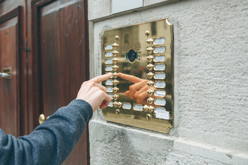 A male hand presses a doorphone button for access inside.