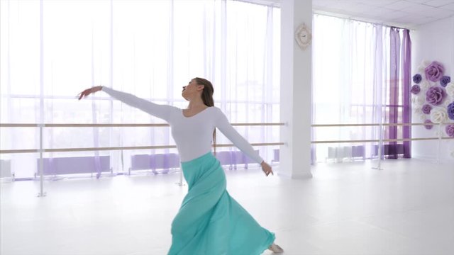 Ballet dancer is rehearsing a dancing elements with jumps and spins. Young ballerina is dancing in long skirt, steadicam shot.