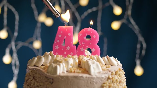 Birthday cake with 48 number pink candle on blue backgraund. Candles are set on fire. Slow motion and close-up view