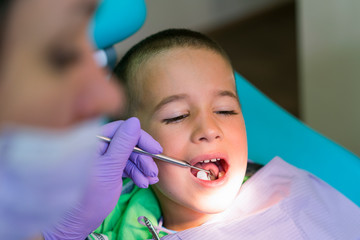 Pediatric dentist examining a little boys teeth in the dentists chair at the dental clinic. A child with a dentist in a dental office. Close up of dentist examination little boy's teeth in clinic