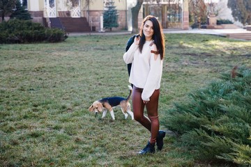 Cute brunette girl is actively spending time with her favorite cute dog. Girl trains on the street dog, breed beagle