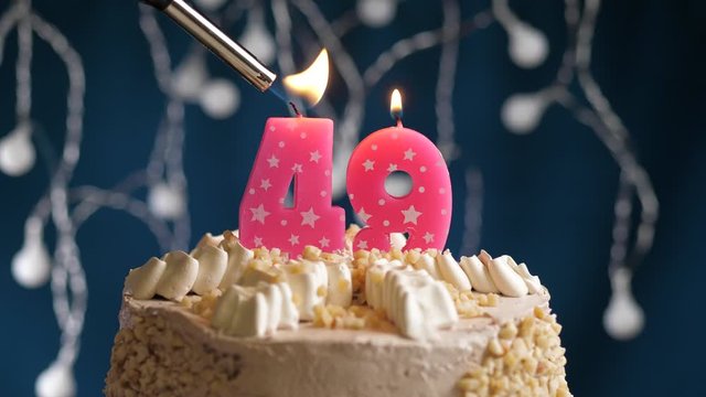 Birthday cake with 49 number pink candle on blue backgraund. Candles are set on fire. Slow motion and close-up view