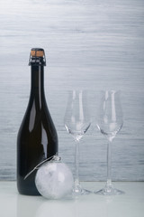 champagne alcoholic drink, in a black bottle, next to two glass glasses and a Christmas-tree decoration ball, on a light gray background