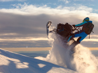 a snowmobile rider jumps in a mountain valley at dawn. sports snow bike with snow splashes and snow...
