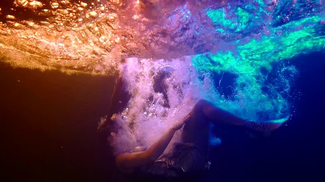 slow motion drop a female body under water in silver clothes in the dark in the light of neons