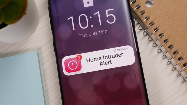 Smartphone showing a home intruder notification banner appearing on the lock screen. Smart home sending a warning alert to the owner during a home burglary.