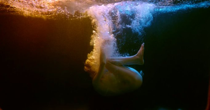 Pathetically plump slender girl under the water in the fetal position in her underwear dark neon lighting