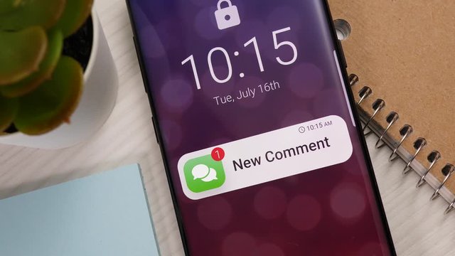 Smartphone showing a new comment notification banner appearing on the lock screen. Mobile phone showing a social media alert.