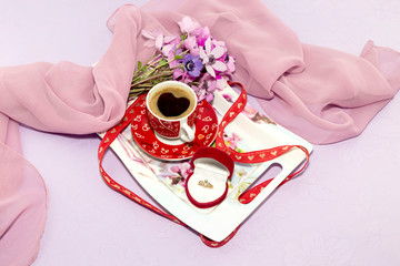 A cup of coffee on a tray, a bouquet of anemones and diamond ring close-up on Valentine's Day.