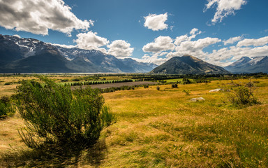 Hiking and treking in wild nature of New Zealand. Summer day over meadow in huge valley with mountains all around.
