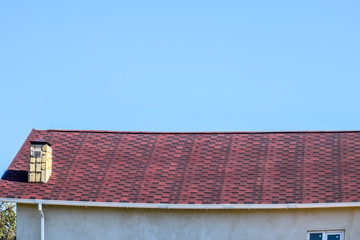 Roof from multi-colored bituminous shingles. Patterned bitumen shingles. Bituminous burgundy roof.